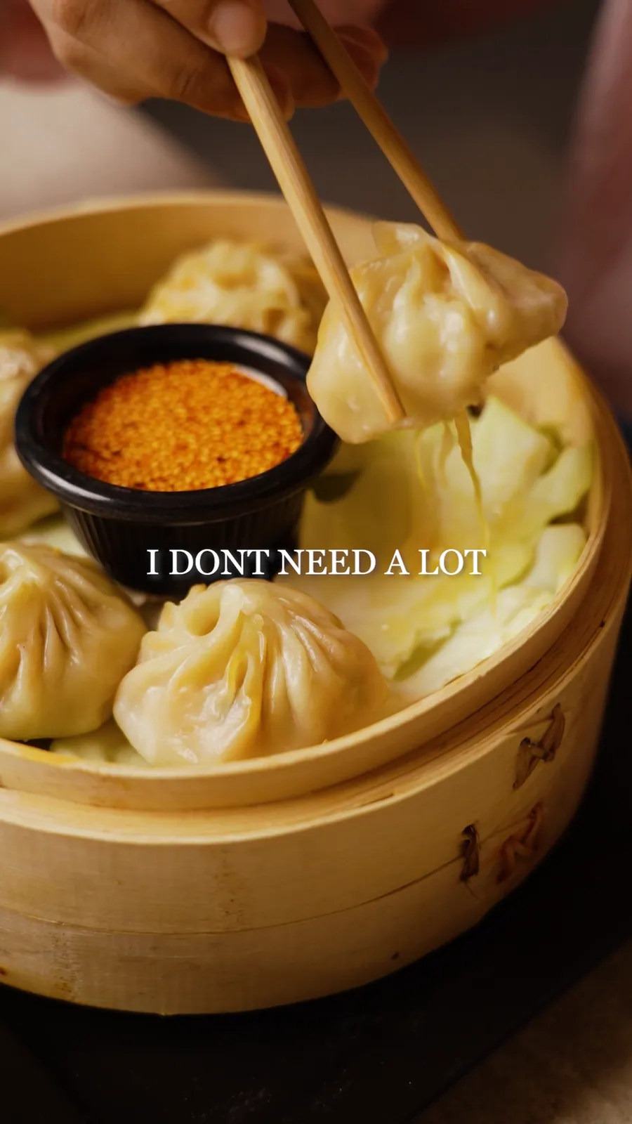 Still from a reel: chopsticks lifting a dumpling from a bamboo steamer beside a bowl of spice, with the words I don't need a lot