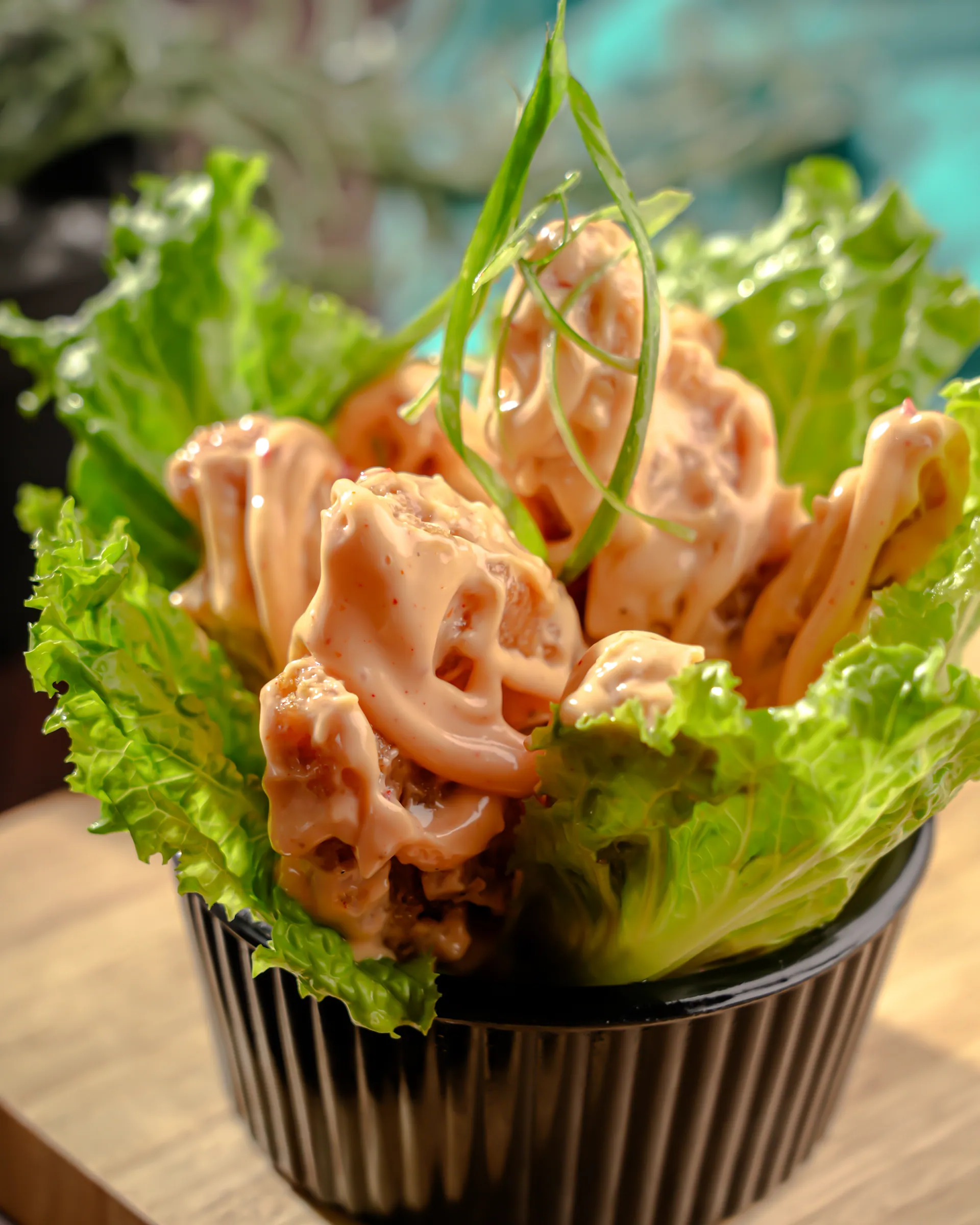 Crisp dynamite prawns piled in a dark bowl on lettuce
