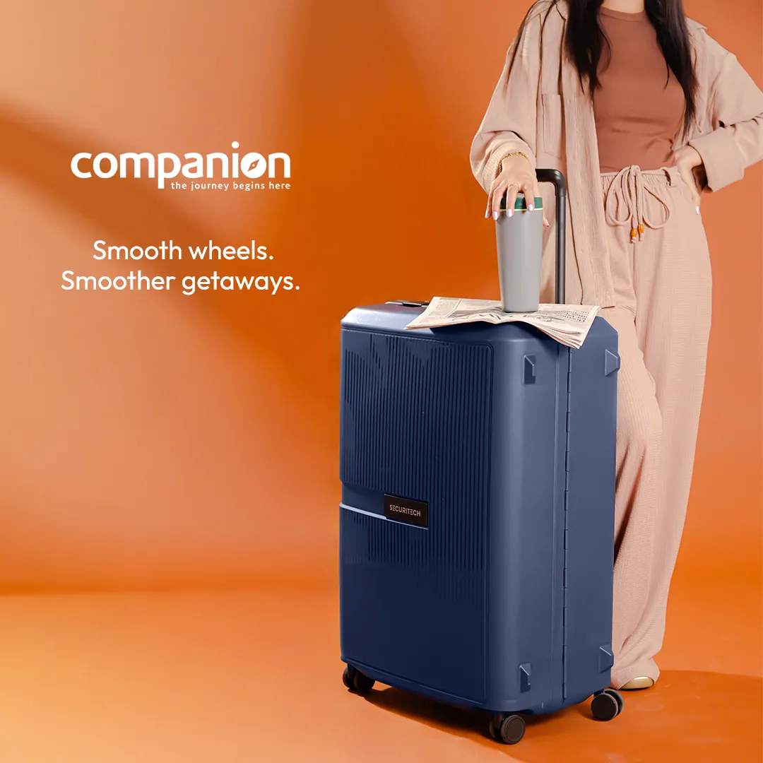 Ad: a navy hard-shell suitcase with a tumbler and a newspaper on top, beside a person in pink, shown from the shoulders down, with the words Smooth wheels. Smoother getaways