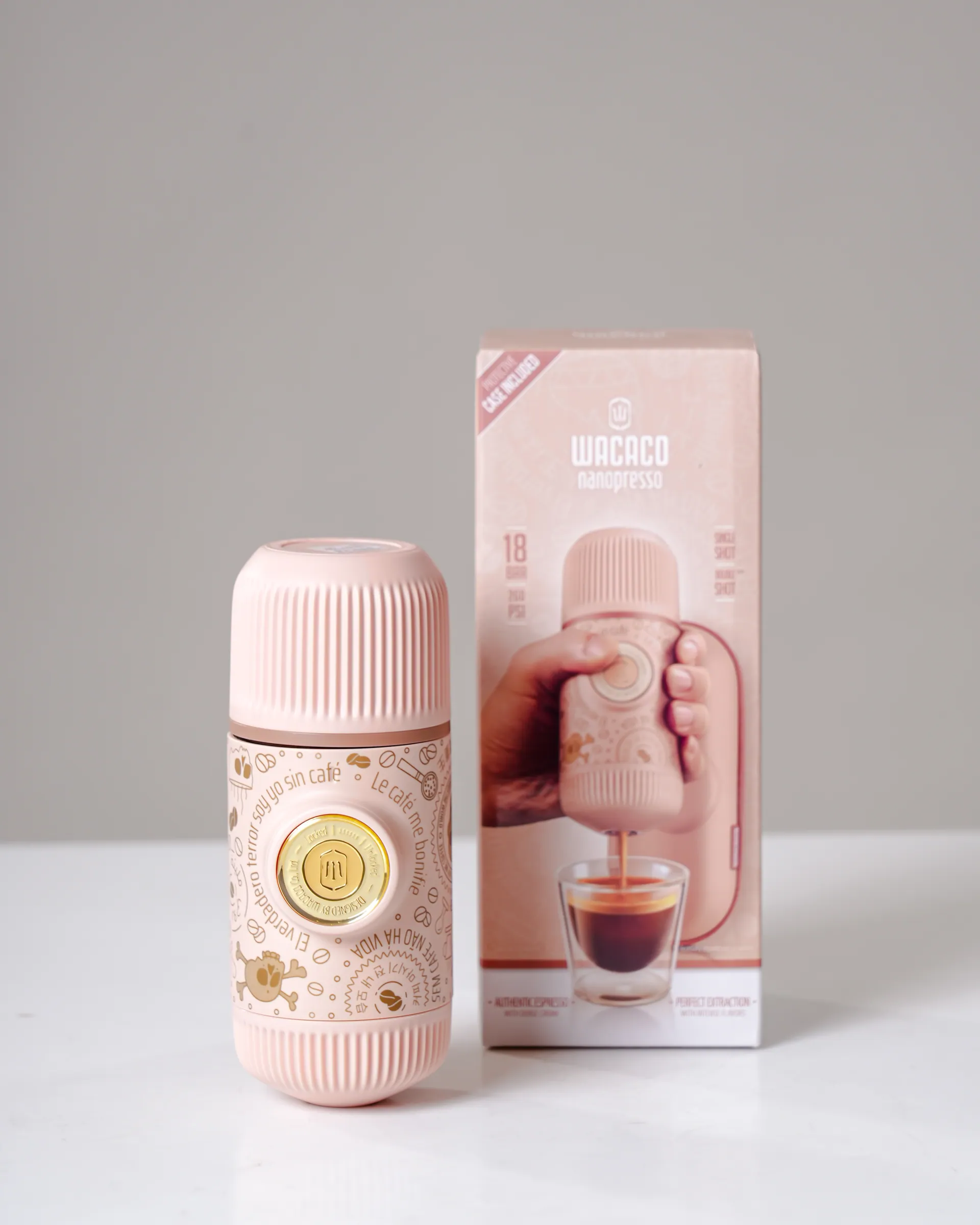 A pink portable coffee maker beside its box, on a pale grey surface