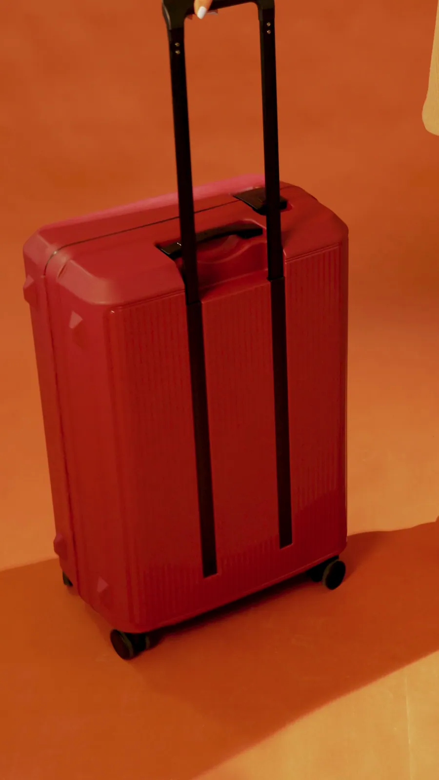 Still from a reel: a red hard-shell suitcase with its handle up, on an orange floor