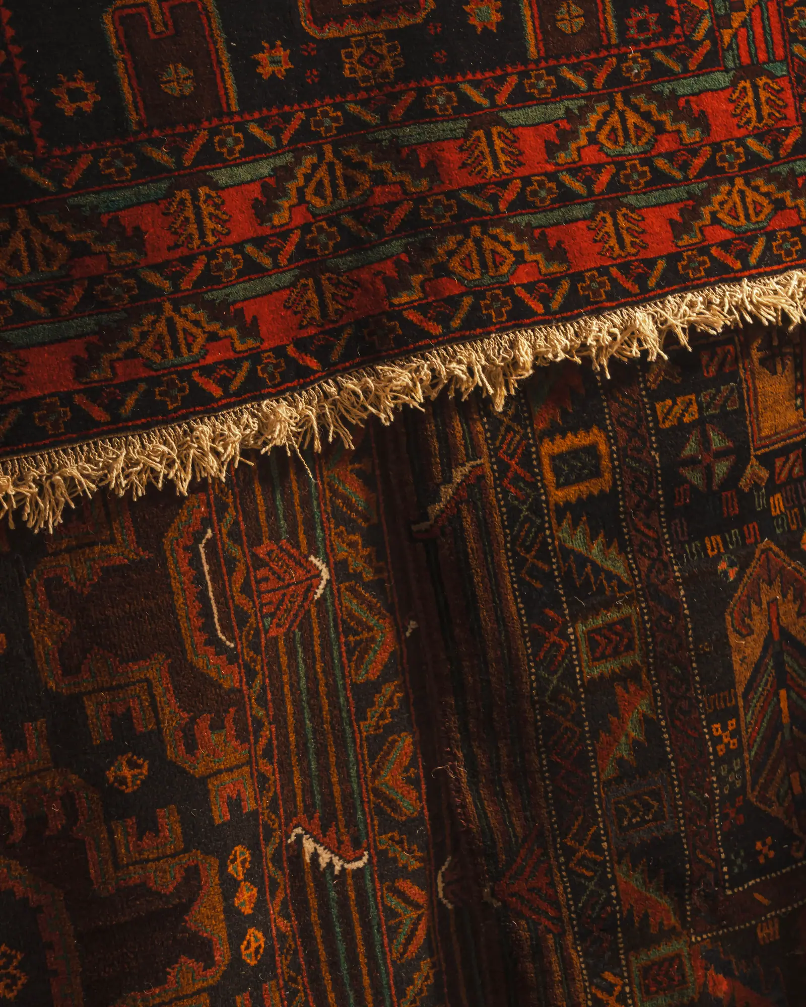 Close-up of a red, black and ochre tribal-pattern rug with a cream fringe, folded over a second patterned rug