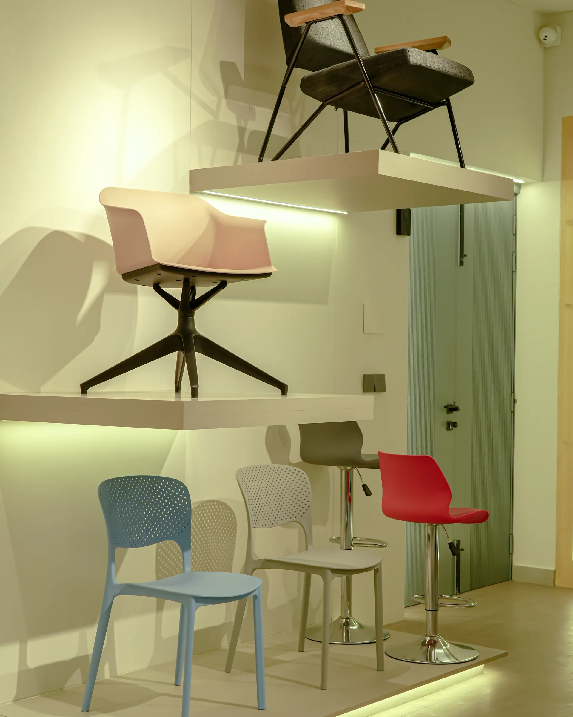 Chairs and bar stools displayed on lit white shelves and on the floor of a showroom