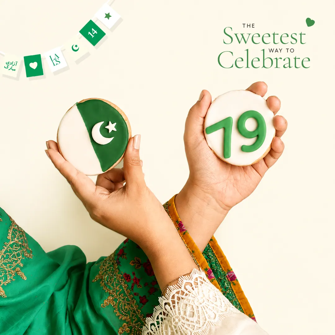 Two hands holding iced cookies, one with a crescent and star and one with the number 79, under green and white bunting