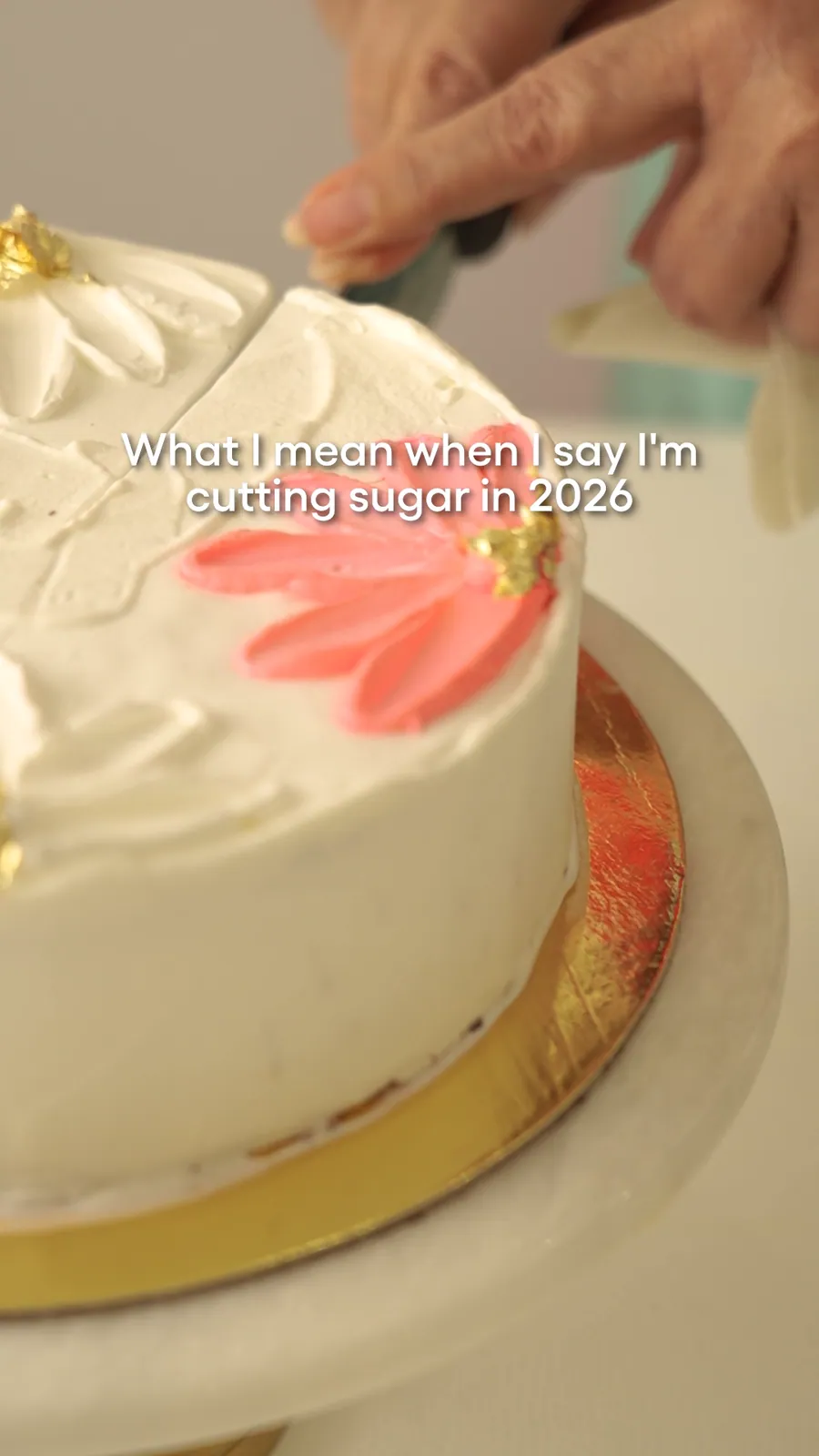 Still from a reel: a knife cutting into a white cake decorated with a pink flower, with the words What I mean when I say I'm cutting sugar in 2026