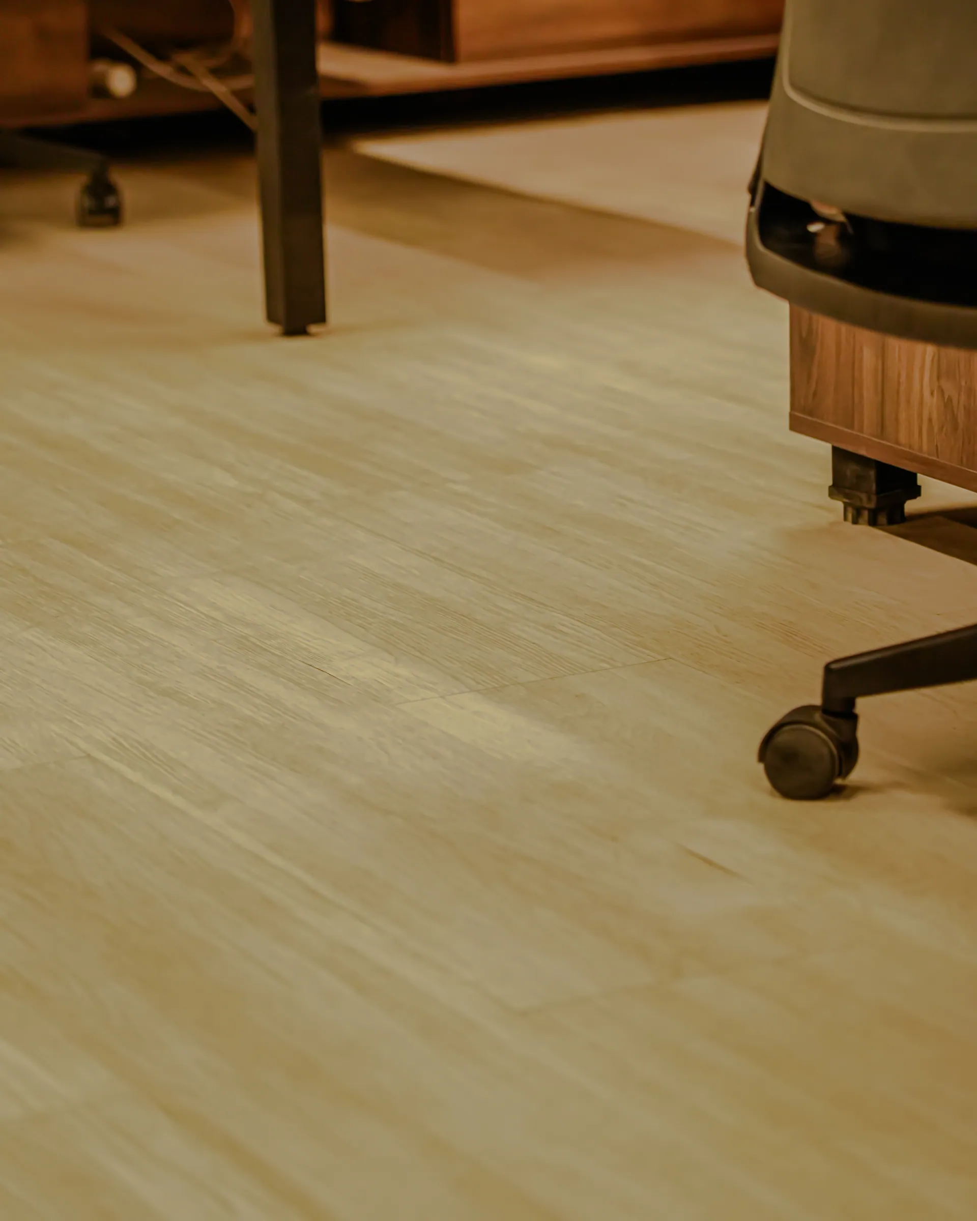 Pale wooden flooring under an office chair and a desk, seen low